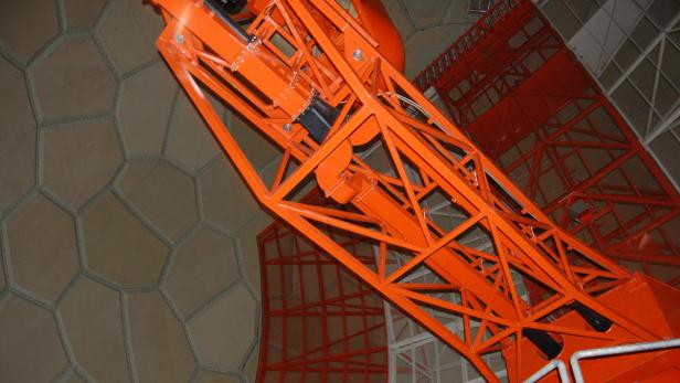 Ein orangefarbenes Teleskop in einer Kuppel mit sechseckigen Paneelen.