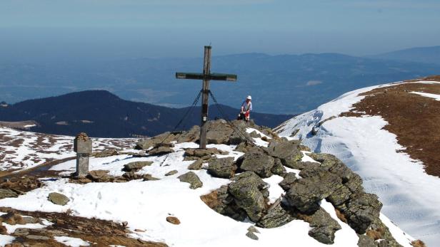 Auf einem schneebedeckten Berggipfel steht ein Holzkreuz.