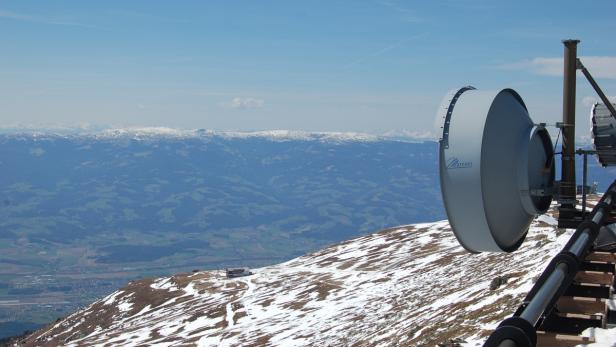Eine Marconi-Antenne auf einem schneebedeckten Berg mit Blick auf eine grüne Landschaft.