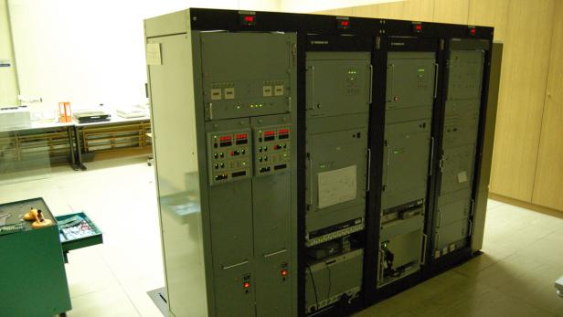 Eine Reihe von grauen Elektronikschränken mit Anzeigen und Bedienelementen in einem Raum.