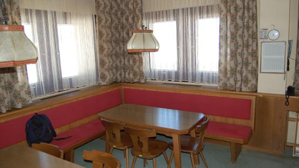 Ein Essbereich mit Holztisch, Stühlen und einer roten Eckbank vor einem Fenster.