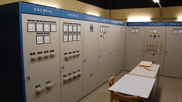 Ein Raum mit Schaltschränken und Messinstrumenten, beschriftet mit „Abzweig“, „Trafo“ und „Generator“.