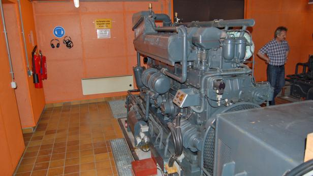 Ein großer Dieselmotor in einem Raum mit orangefarbenen Wänden und einem Mann im Hintergrund.