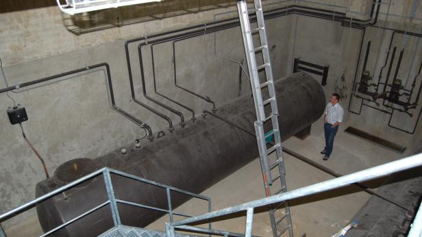 Ein Mann steht in einem Raum mit einem großen Tank und vielen Rohren an den Wänden.