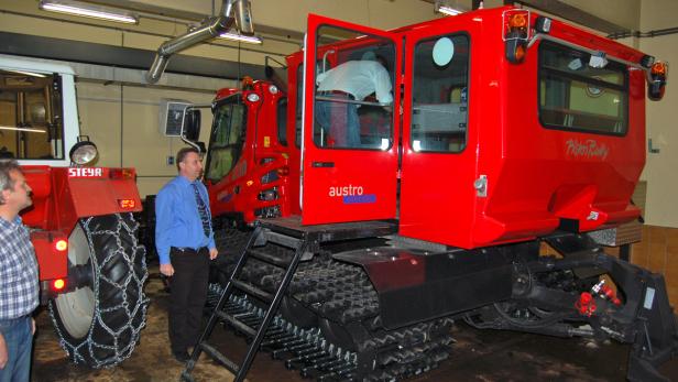 Zwei Männer betrachten eine rote Pistenraupe der Marke PistenBully.