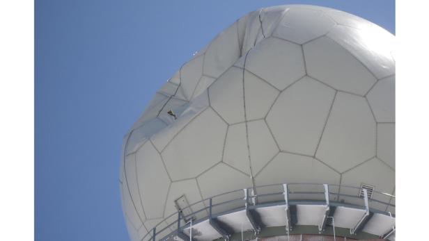 Eine Radarkuppel mit einer beschädigten Stelle vor blauem Himmel.