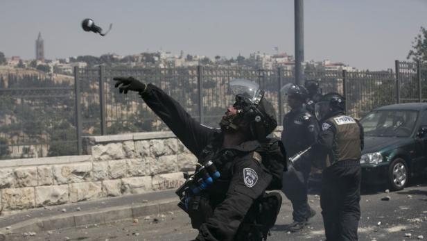 Ein Polizist wirft eine Tränengasgranate in einer städtischen Umgebung.