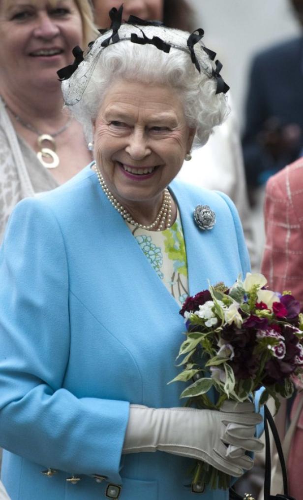 Königin Elisabeth II. lächelt und hält einen Blumenstrauß.