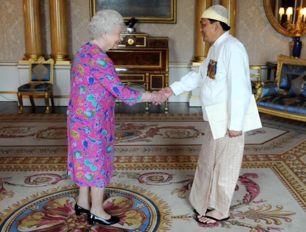Königin Elisabeth II. schüttelt einem Mann in traditioneller burmesischer Kleidung die Hand.