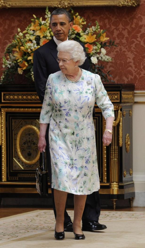 Königin Elisabeth II. und Barack Obama stehen in einem Raum mit Blumenarrangements.