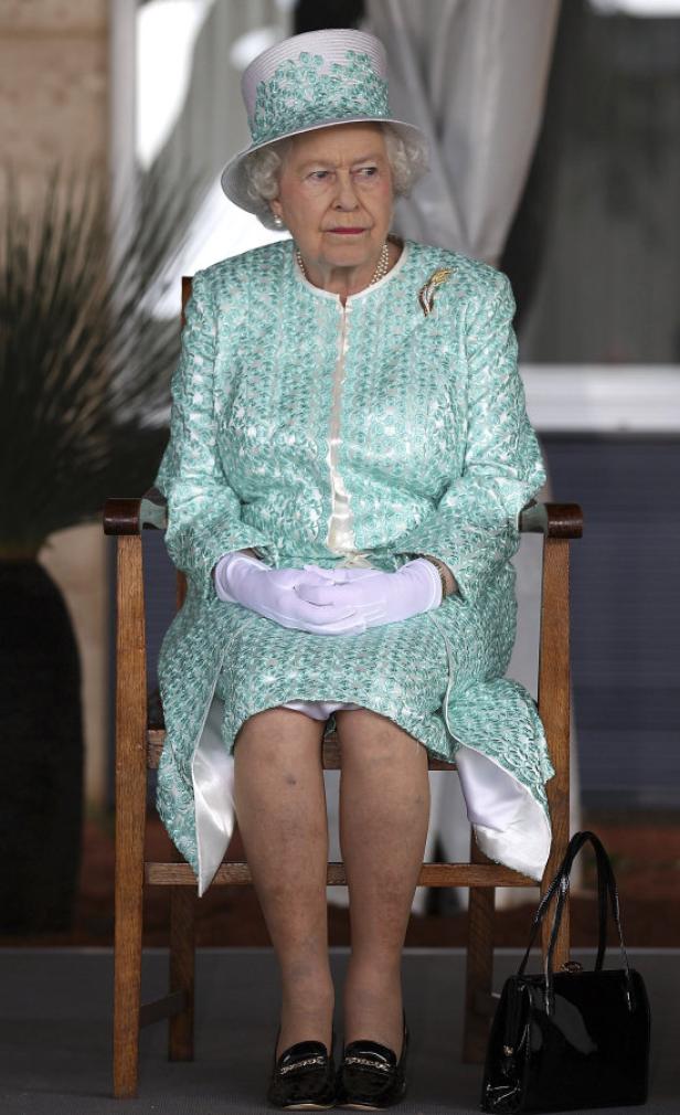 Königin Elisabeth II. sitzt auf einem Stuhl und trägt ein hellgrünes Kostüm mit passendem Hut.