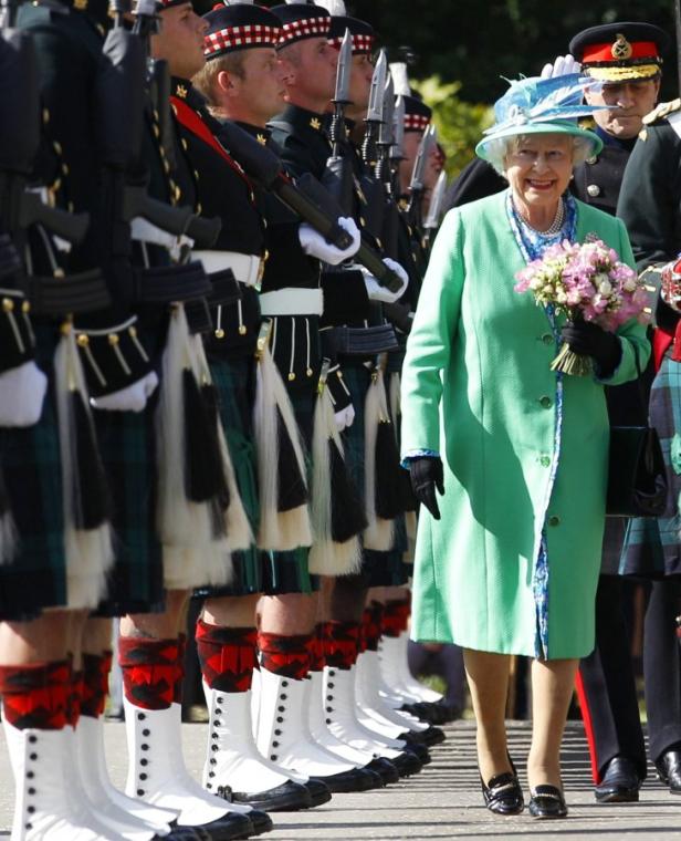 Königin Elisabeth II. mit einem Blumenstrauß neben einer Reihe von Soldaten in Kilts.