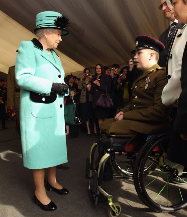 Königin Elisabeth II. spricht mit einem im Rollstuhl sitzenden Soldaten.