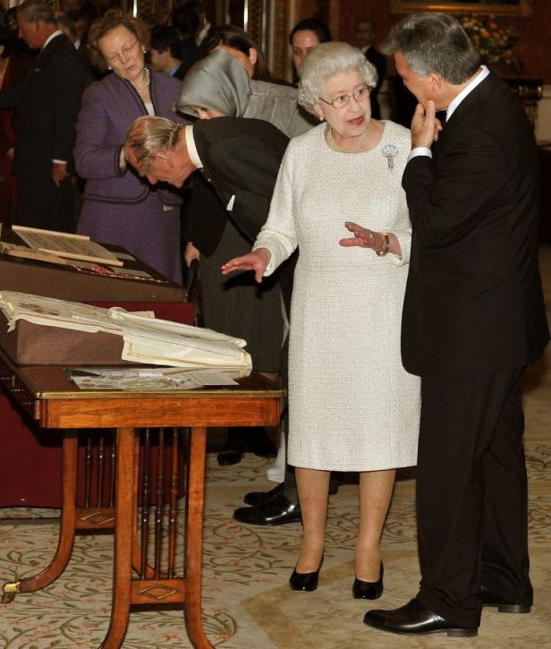 Königin Elisabeth II. gestikuliert, während sie sich mit einem Mann unterhält.