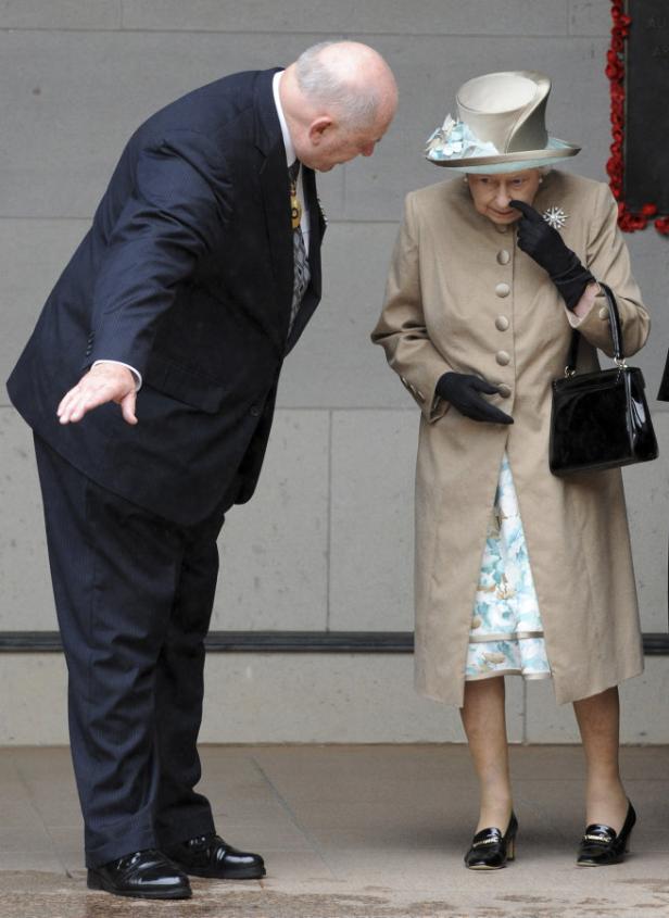 Königin Elizabeth II. mit einem Mann, der sich zu ihr herunterbeugt.