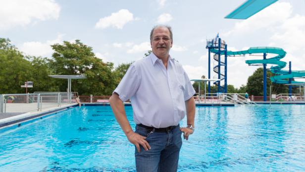Ein Mann steht vor einem Schwimmbecken mit Rutsche und Sprungturm im Hintergrund.