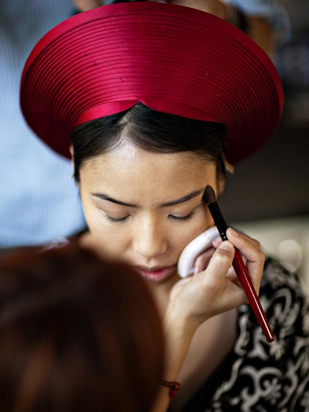 Eine Frau mit rotem Hut bekommt Make-up aufgetragen.