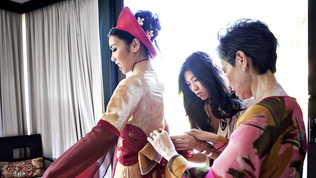Eine junge Frau wird von zwei Helferinnen in ein traditionelles vietnamesisches Kleid gekleidet.