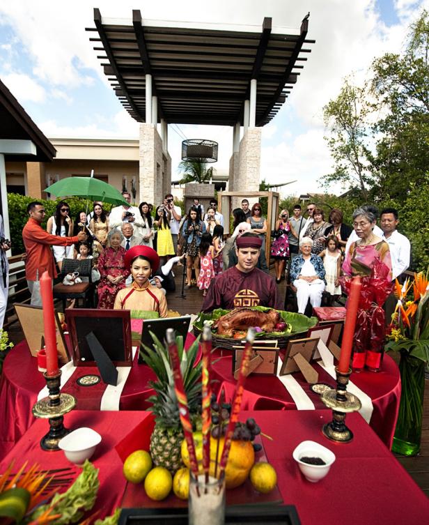 Ein Paar in traditioneller vietnamesischer Kleidung sitzt vor einem Tisch mit Opfergaben während einer Zeremonie.