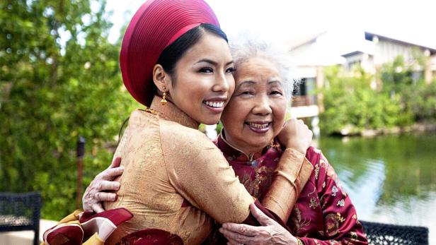 Eine junge Frau im traditionellen vietnamesischen Ao Dai umarmt ihre ältere Mutter oder Großmutter.