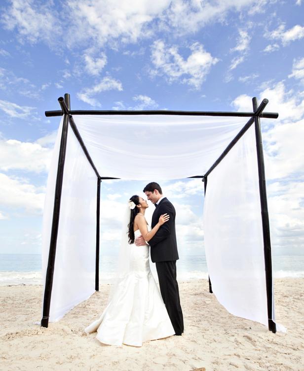Ein Brautpaar umarmt sich unter einem Baldachin am Strand.