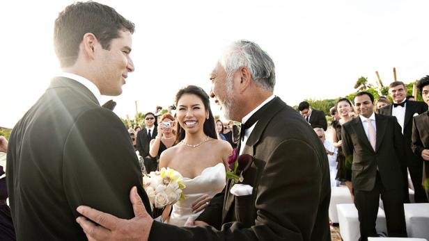 Eine Braut mit ihrem Vater und dem Bräutigam während einer Hochzeitszeremonie im Freien.