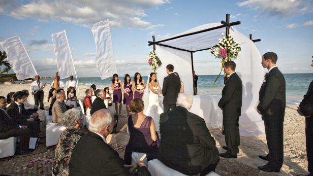 Eine Hochzeit findet am Strand unter einem weißen Baldachin statt.