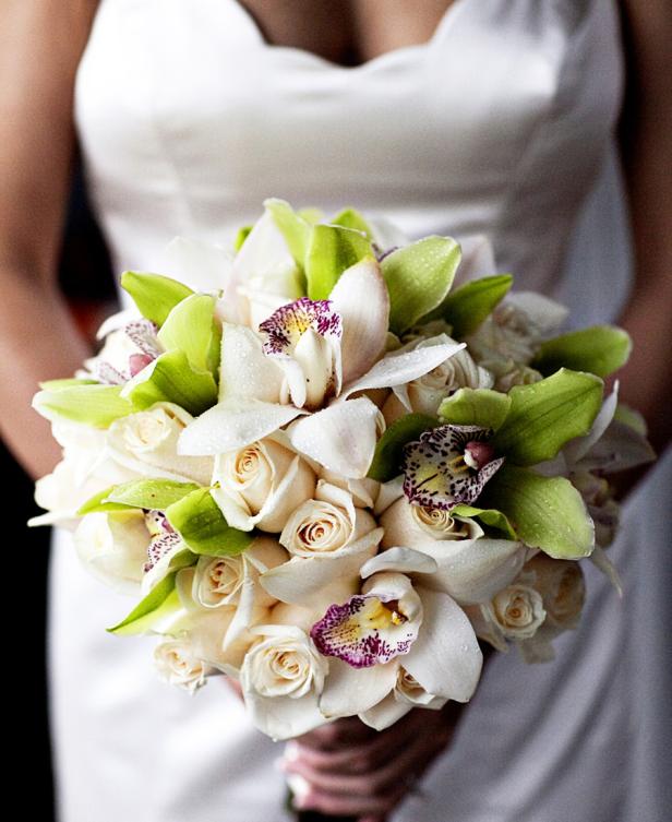 Eine Braut hält einen üppigen Brautstrauß aus Rosen und Orchideen.