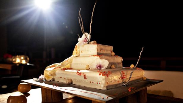 Ein dekorativer, mehrstöckiger Kuchen mit Blumen und Ornamenten steht im Dunkeln.