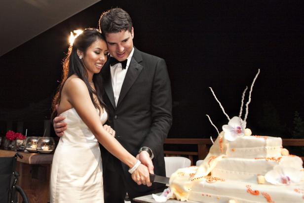 Ein Brautpaar schneidet gemeinsam eine Hochzeitstorte an.