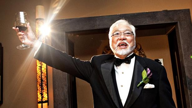 Ein Mann im Smoking mit Fliege hebt ein Glas Rotwein.