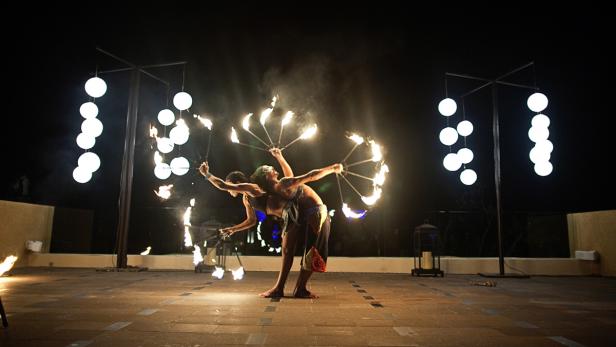 Zwei Feuerkünstler treten mit brennenden Fächern vor einem dunklen Hintergrund auf.