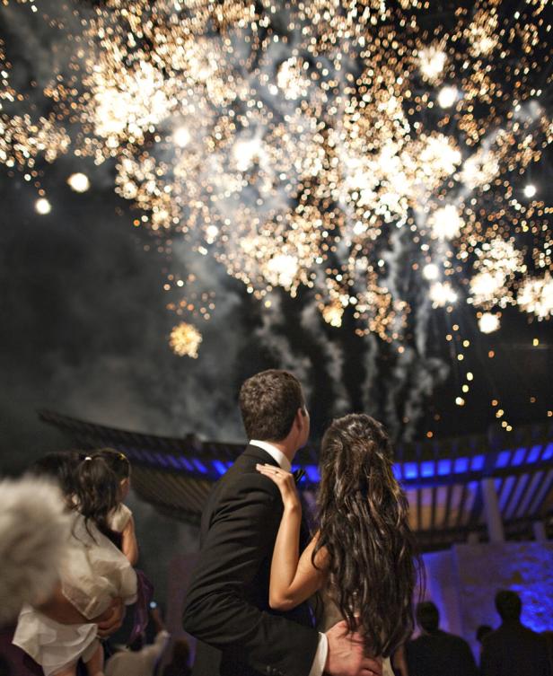 Ein Brautpaar betrachtet ein Feuerwerk am Nachthimmel.