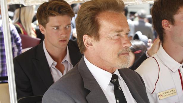 Arnold Schwarzenegger in einem Golfwagen mit anderen Personen.