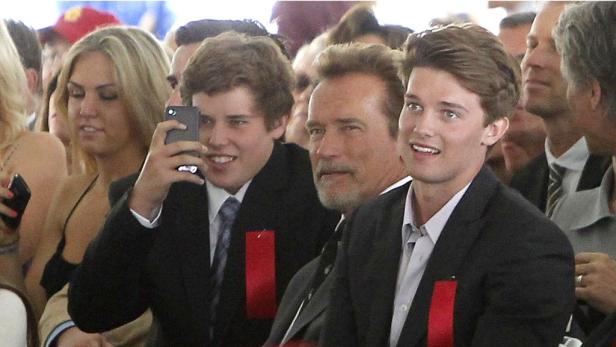 Arnold Schwarzenegger posiert mit zwei jungen Männern für ein Foto.
