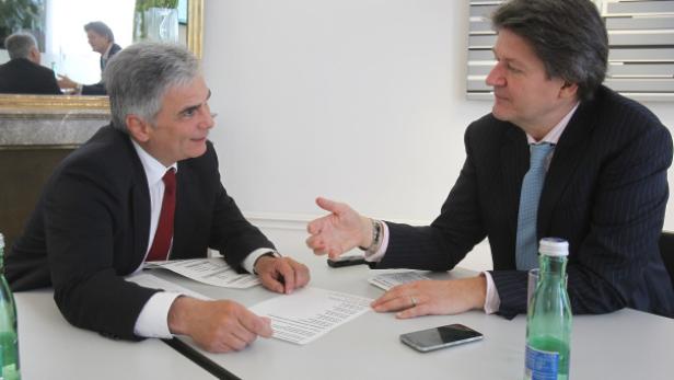 Zwei Männer in Anzügen sitzen an einem Tisch und diskutieren.