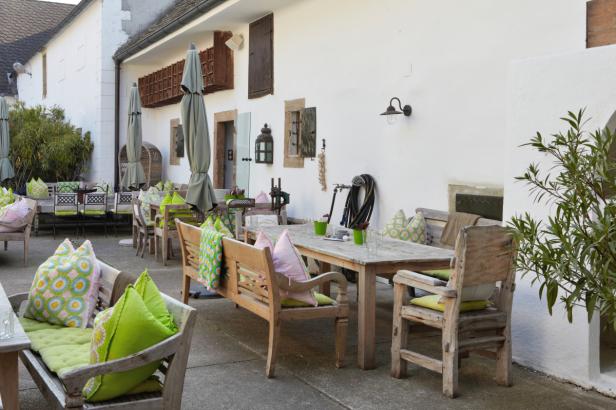 Einladender Außenbereich eines Restaurants mit Holztischen und bunten Kissen.