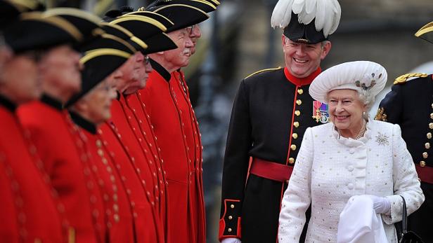 Königin Elizabeth II. lächelt neben einer Reihe von Yeomen of the Guard.