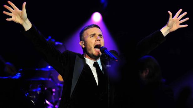 Gary Barlow singt mit erhobenen Armen auf einer Bühne.