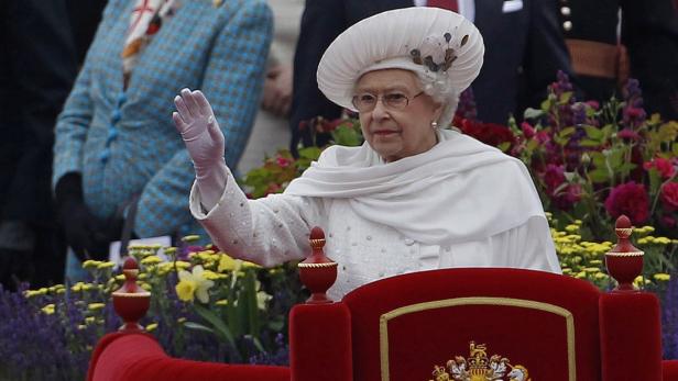 Königin Elisabeth II. winkt in einem weißen Outfit und Hut.