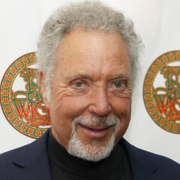 Porträt von Tom Jones mit grauem Haar und Bart vor einem verzierten Hintergrund.