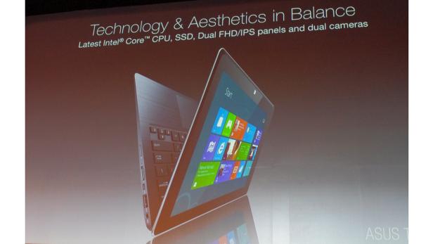 Ein geöffnetes ASUS-Notebook mit Windows-Startbildschirm wird auf einer Präsentation gezeigt.