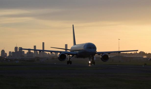 Ein Flugzeug landet bei Sonnenuntergang auf einer Landebahn vor einer Stadtkulisse.