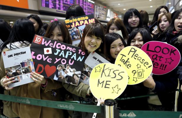 Eine Gruppe junger Fans hält Schilder für die Band One Direction in Japan hoch.