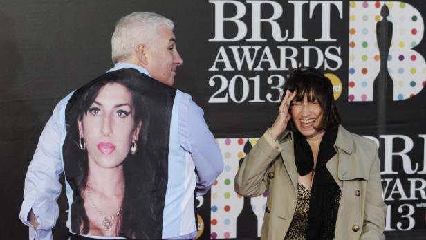 Ein Mann mit einer Weste mit einem Bild von Amy Winehouse und eine lachende Frau bei den Brit Awards 2013.