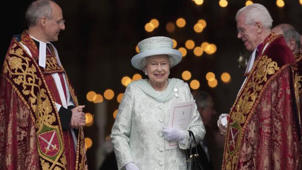 Königin Elisabeth II. lächelt zwischen zwei Geistlichen.