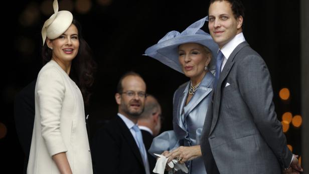 Drei elegant gekleidete Personen, darunter zwei Frauen mit Hüten, posieren für ein Foto.