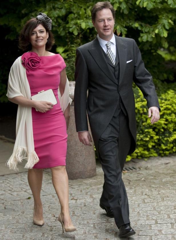 Ein Mann im Anzug und eine Frau in einem pinkfarbenen Kleid gehen zusammen auf einem gepflasterten Weg.