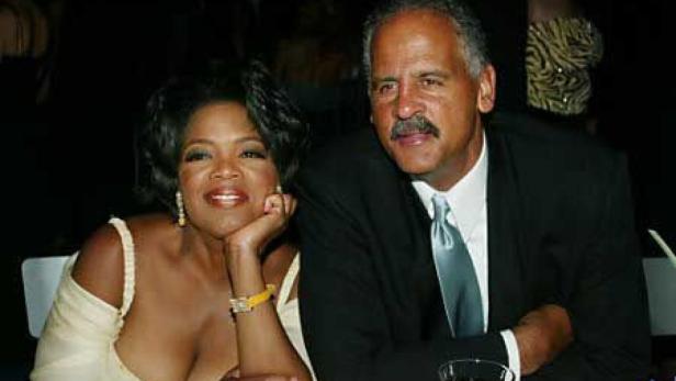 Oprah Winfrey sitzt mit einem Mann im Anzug an einem Tisch.