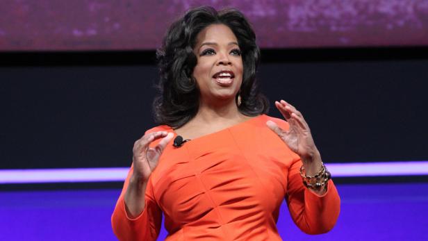 Oprah Winfrey spricht auf einer Bühne in einem orangefarbenen Kleid.
